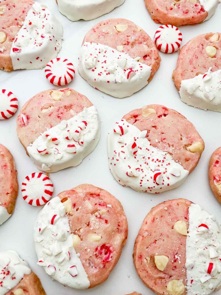 White Chocolate Peppermint Shortbread cookies spread out on a white counter with round peppermints.