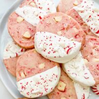 Closer view of pink White Chocolate Peppermint Shortbread cookies in a pile on a white plate.