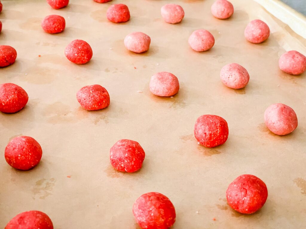 Balls of red and pink dough on a baking sheet.