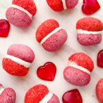 Looking down on pink and red Valentine's Day Baci di Dama Cookies on a counter with some red hearts.