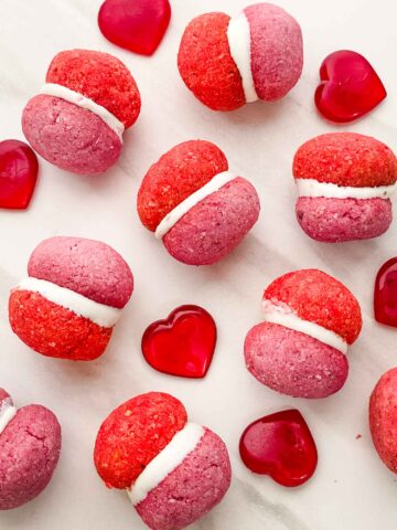 Looking down on pink and red Valentine's Day Baci di Dama Cookies on a counter with some red hearts.