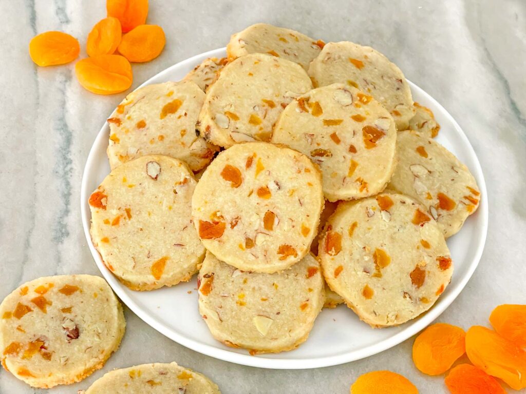 A plate of Apricot Almond Shortbread Cookies on a counter with dried fruit around it.