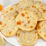 A white plate full of Apricot Almond Shortbread Cookies in a pile and sitting on a counter.