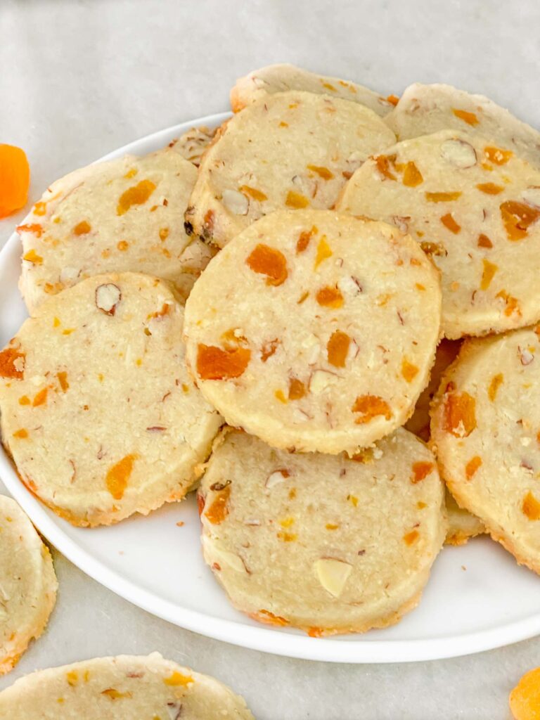 A white plate full of Apricot Almond Shortbread Cookies in a pile and sitting on a counter.