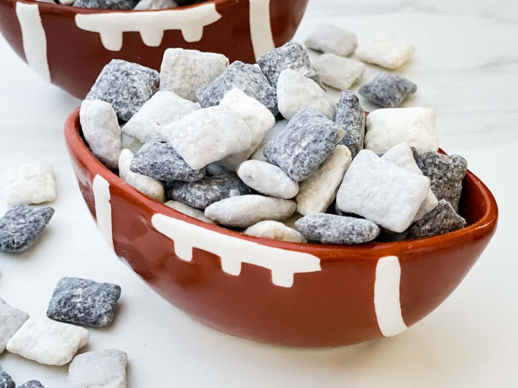 A football bowl full of black, gray, and white Las Vegas Raiders Puppy Chow on a counter.
