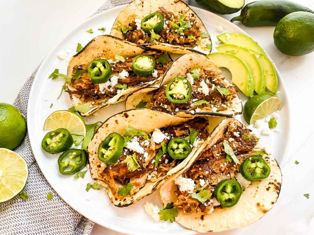 A plate with five Pulled Pork Carnitas Street Tacos on it on a counter.