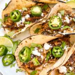 A closer view of Pulled Pork Carnitas Street Tacos stacked next to each other.