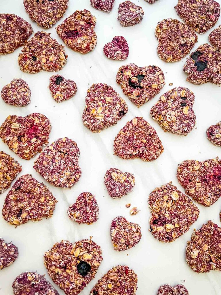 Patterns of heart shaped Crunchy Berry Parfait Dog Treats on a counter.