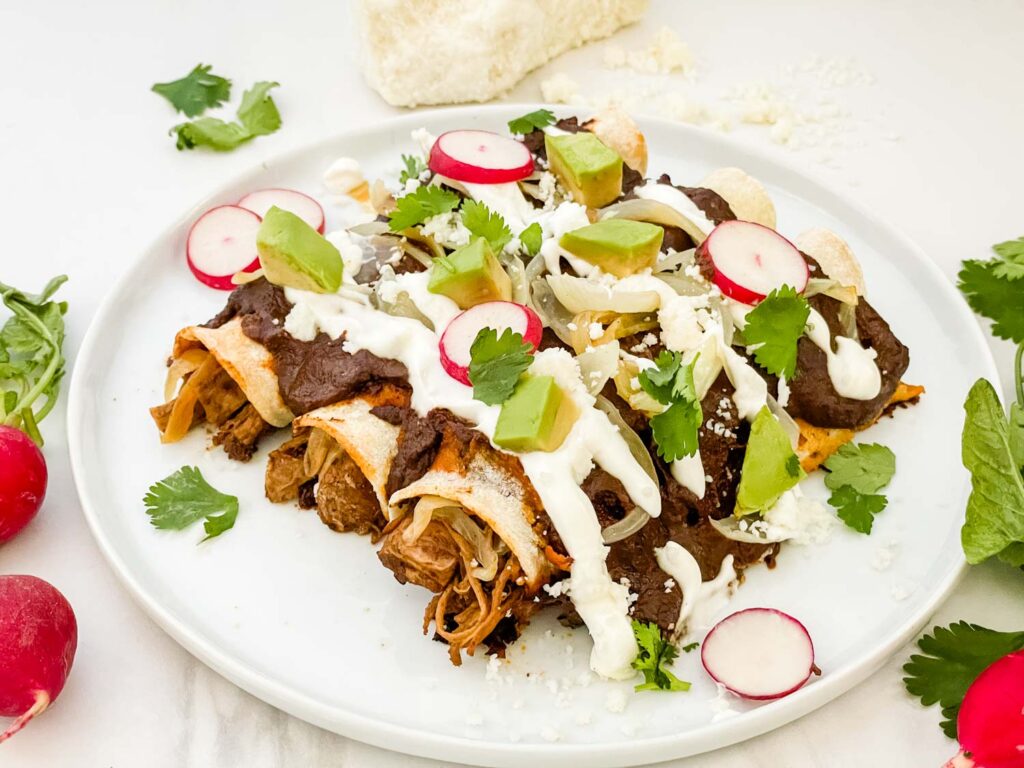 Three Chicken Mole Enchiladas on a white plate with radishes, sour cream, and fresh cilantro.