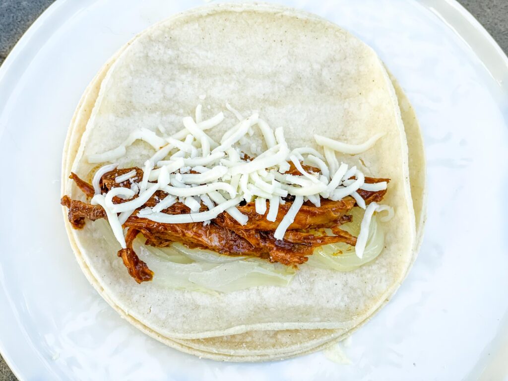 A flat corn tortilla with the onions, chicken, and cheese before being rolled up.