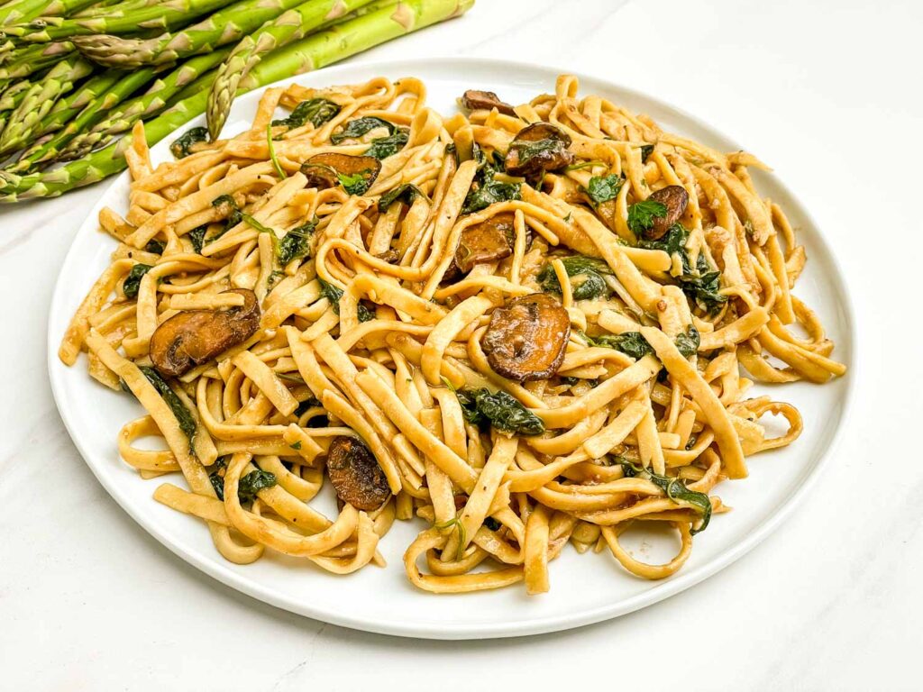 A plate of fettuccine pasta with Mushroom Marsala Wine Sauce on a counter with asparagus.