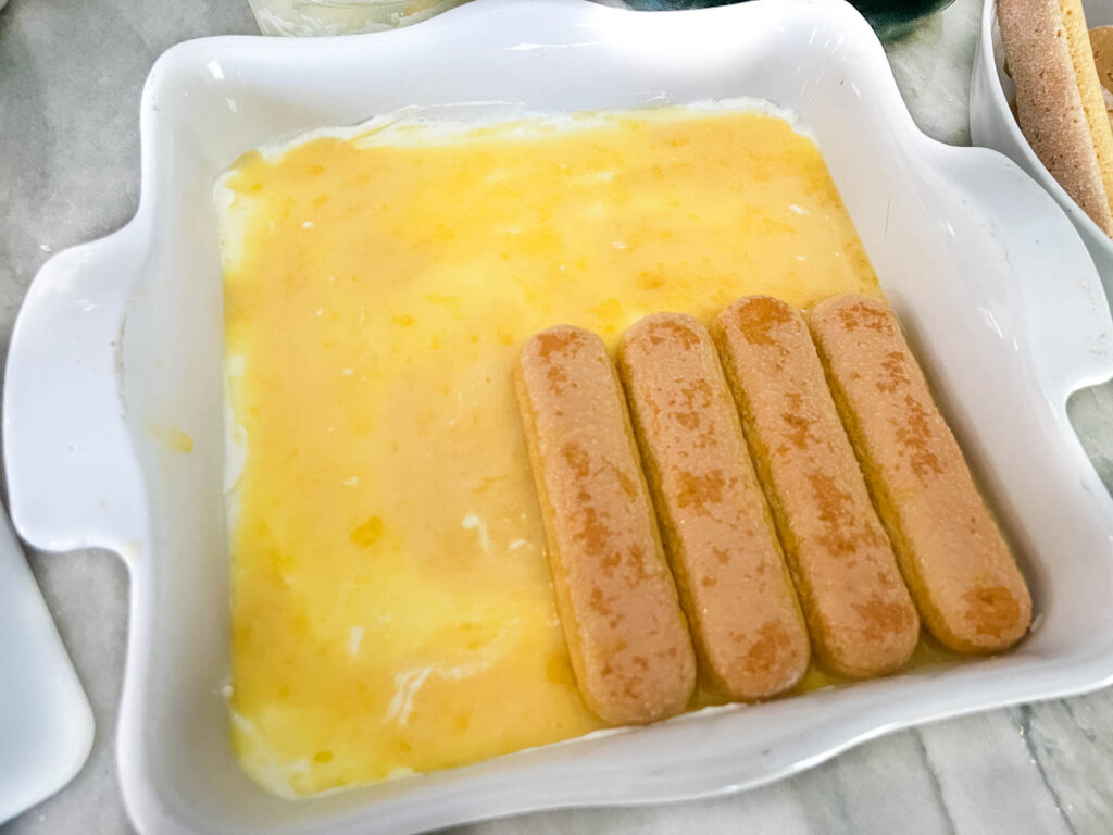 Lady fingers starting to be added to the bottom layer of the dessert.
