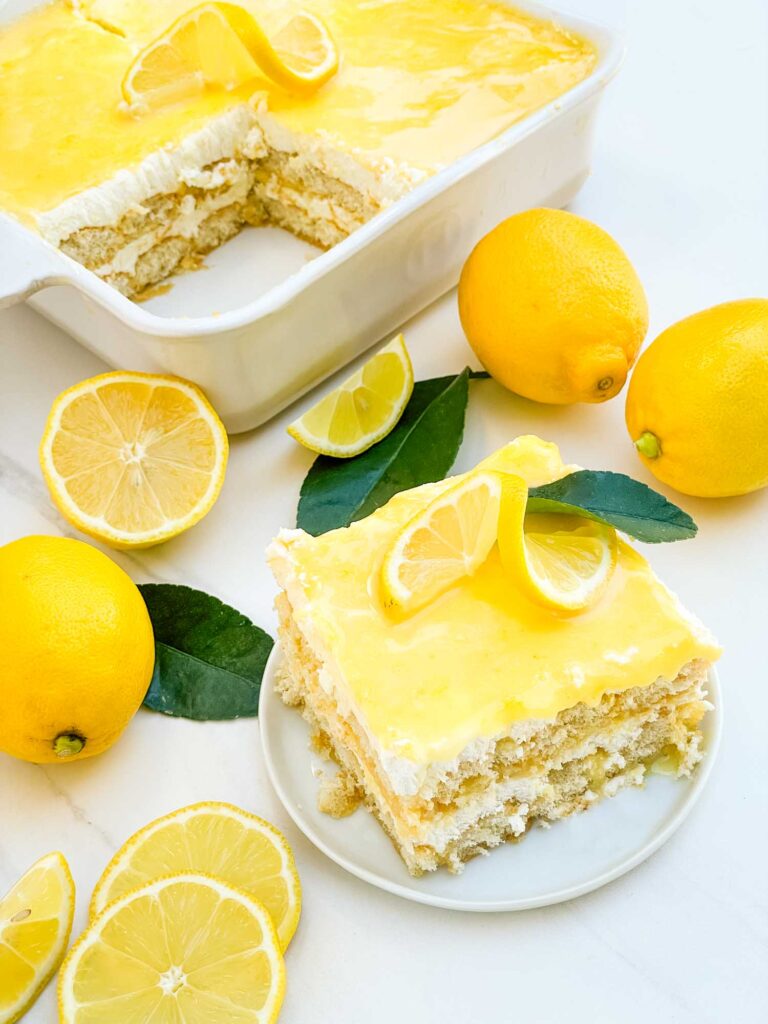 Looking down on the Limoncello Tiramisu dish with a piece on a plate next to it, all surrounded by fresh lemons.