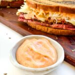 A small bowl of Russian Dressing Recipe (for Reuben Sandwich) in front of a sandwich.