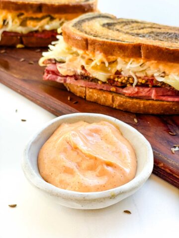A small bowl of Russian Dressing Recipe (for Reuben Sandwich) in front of a sandwich.