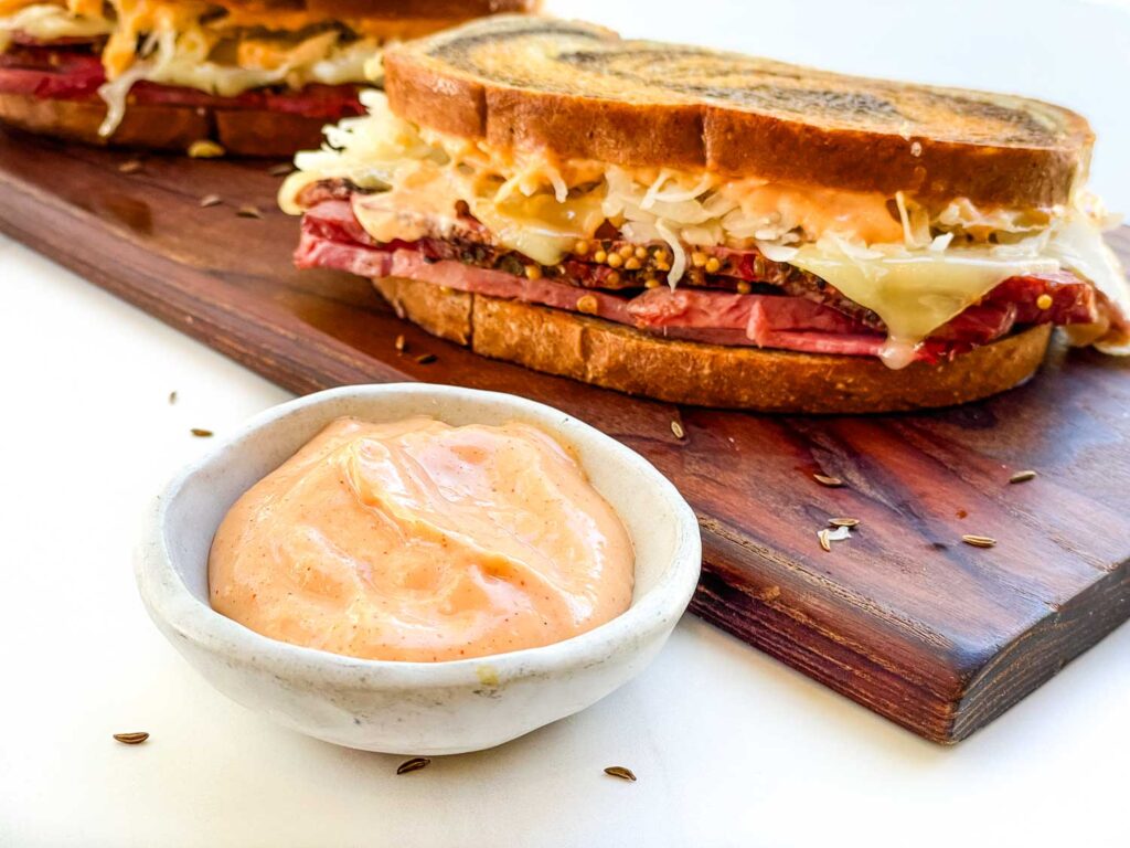 A small bowl of Russian Dressing Recipe (for Reuben Sandwich) with a sandwich.