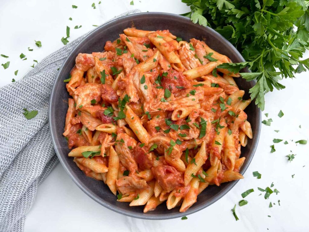 Looking down on a gray bowl full of Chicken alla Vodka Pasta on a counter with a fresh parsley garnish.