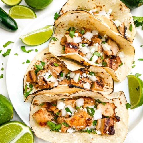 Looking down on four Chicken Street Tacos on a plate surrounded by limes.