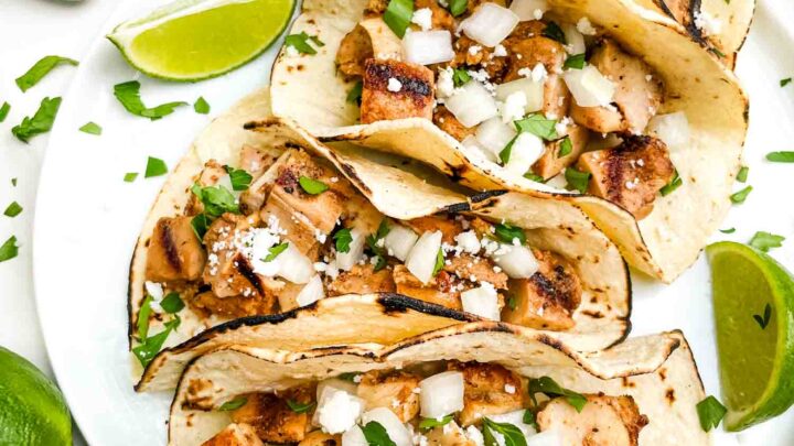 Looking down on four Chicken Street Tacos on a plate surrounded by limes.