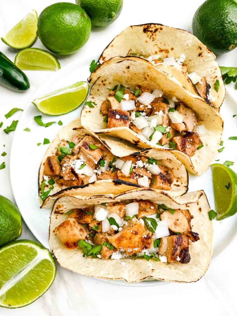 Looking down on four Chicken Street Tacos on a plate surrounded by limes.