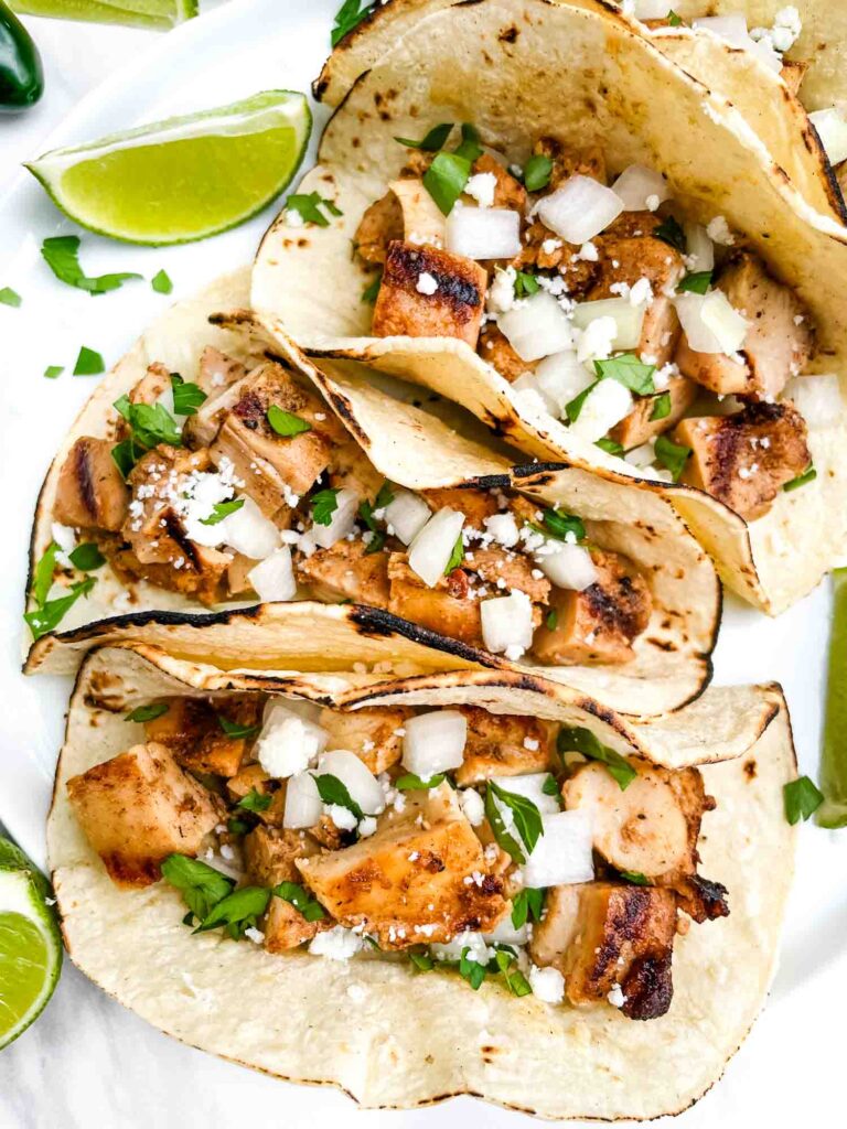 Looking down closely on four Chicken Street Tacos on a white plate.