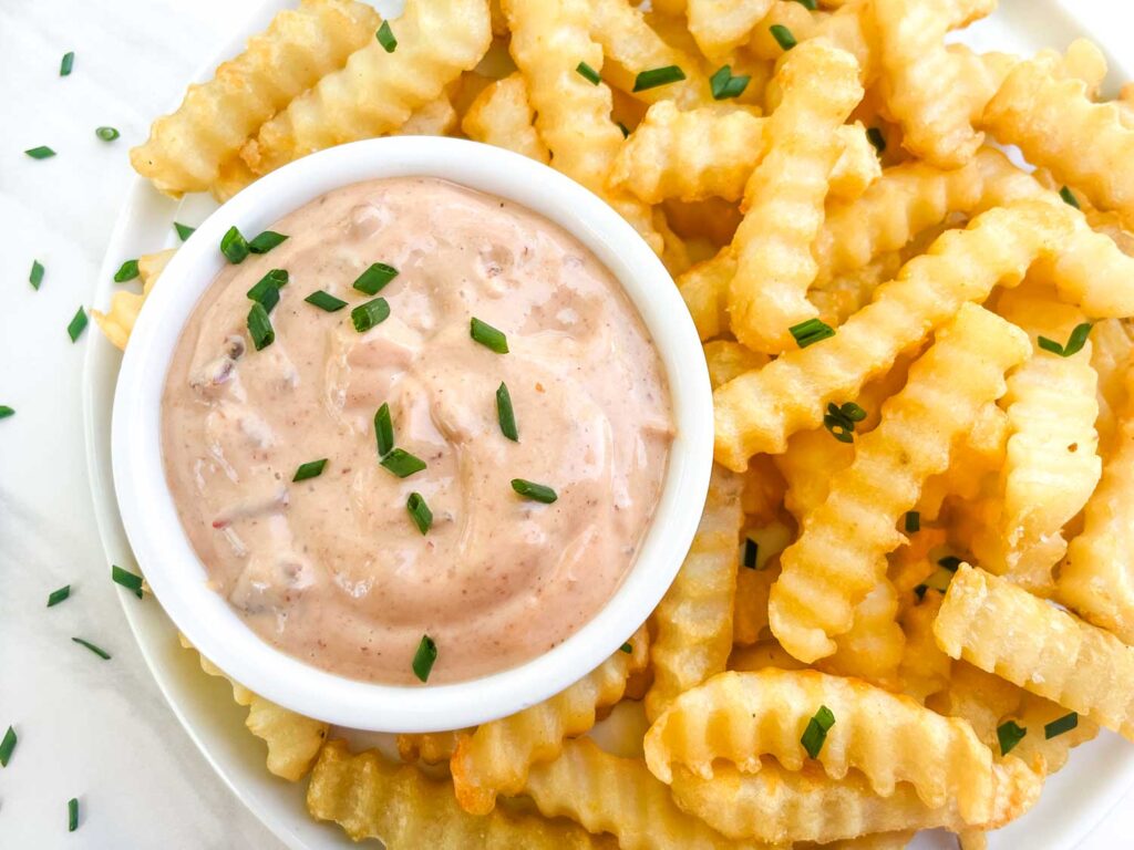 Looking down on a small bowl of Homemade Chipotle Aioli Sauce surrounded by french fries.