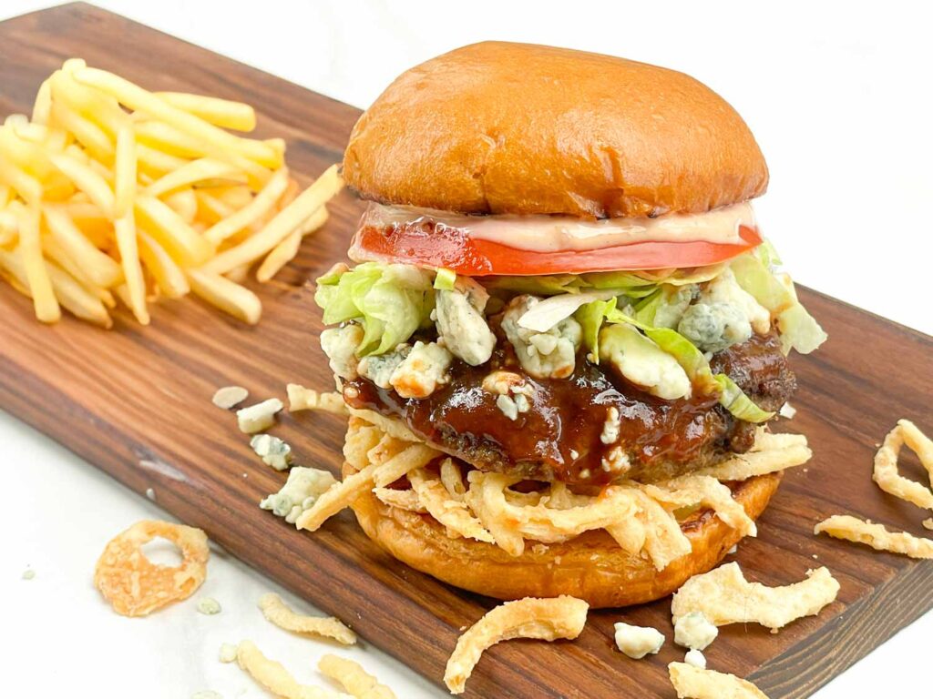 A Copycat Red Robin Bleu Ribbon Burger sitting on a wood board with some french fries.