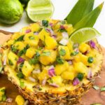 Pin looking down on a bowl made out of hollowed pineapple and full of Pineapple Mango Salsa with title at top.