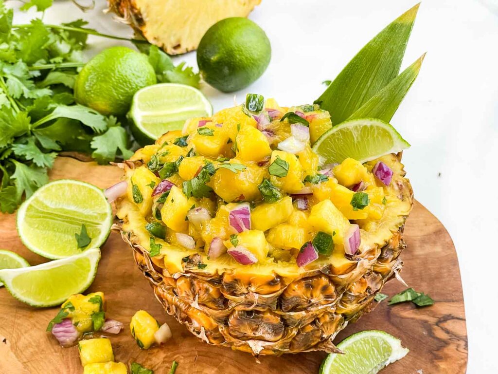Pineapple Mango Salsa inside a hollowed out bowl made of pineapple sitting on a wood board.