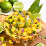 Pineapple Mango Salsa sitting inside a scooped out pineapple bowl on a wood board with fresh limes.