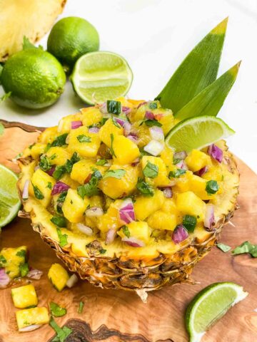 Pineapple Mango Salsa sitting inside a scooped out pineapple bowl on a wood board with fresh limes.