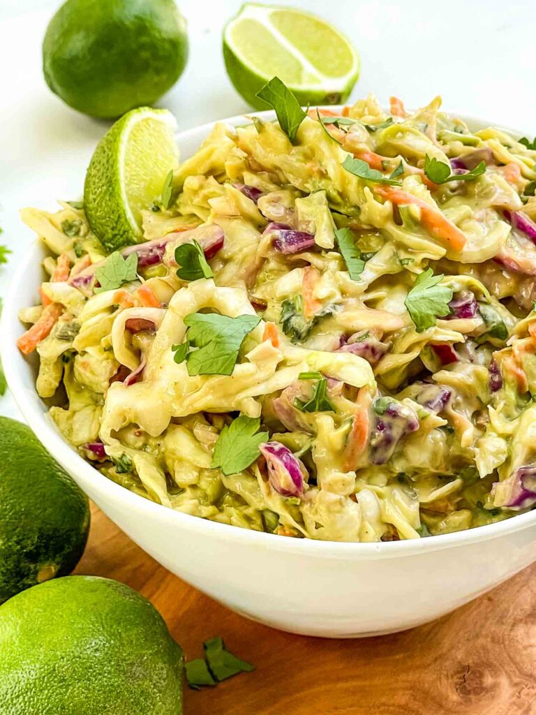 Looking closely at a bowl of Creamy Avocado Coleslaw (without Mayo) with fresh limes around it.