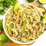 Looking down at a white bowl of Creamy Avocado Coleslaw (without Mayo) on a wood board on a counter.