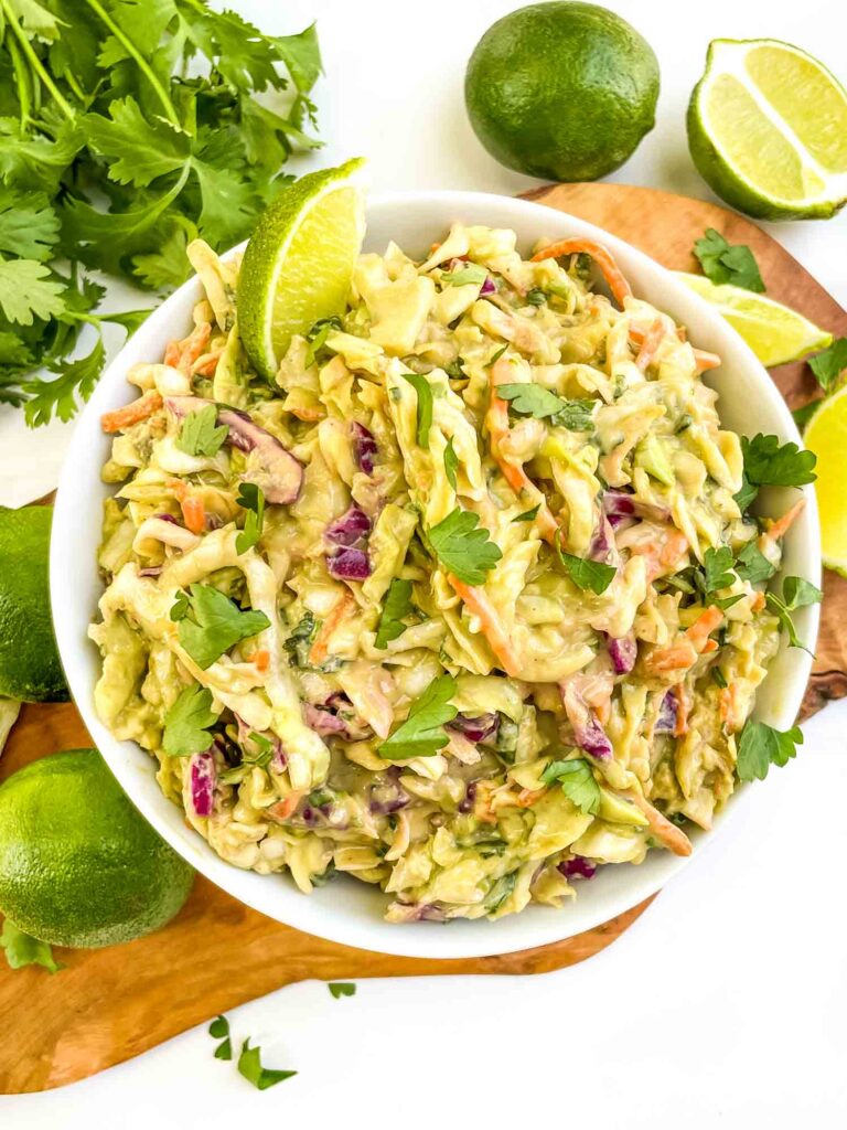 Looking down at a white bowl of Creamy Avocado Coleslaw (without Mayo) on a wood board on a counter.