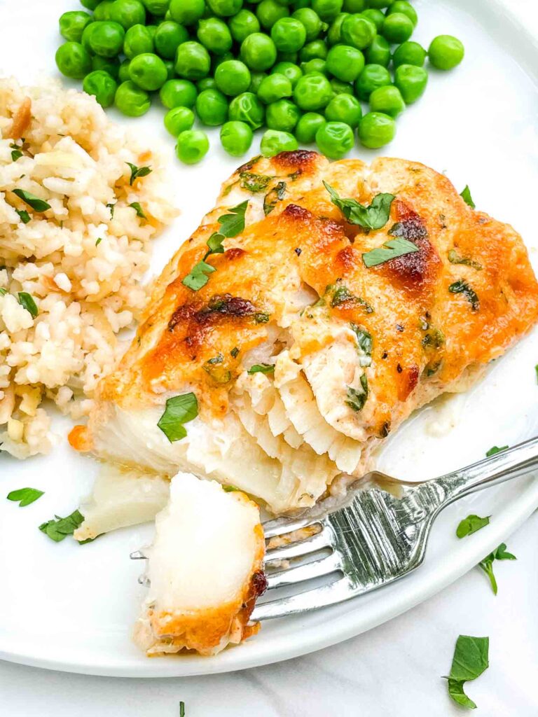 A fork having taking a piece out of a Parmesan Baked Cod on a white plate.