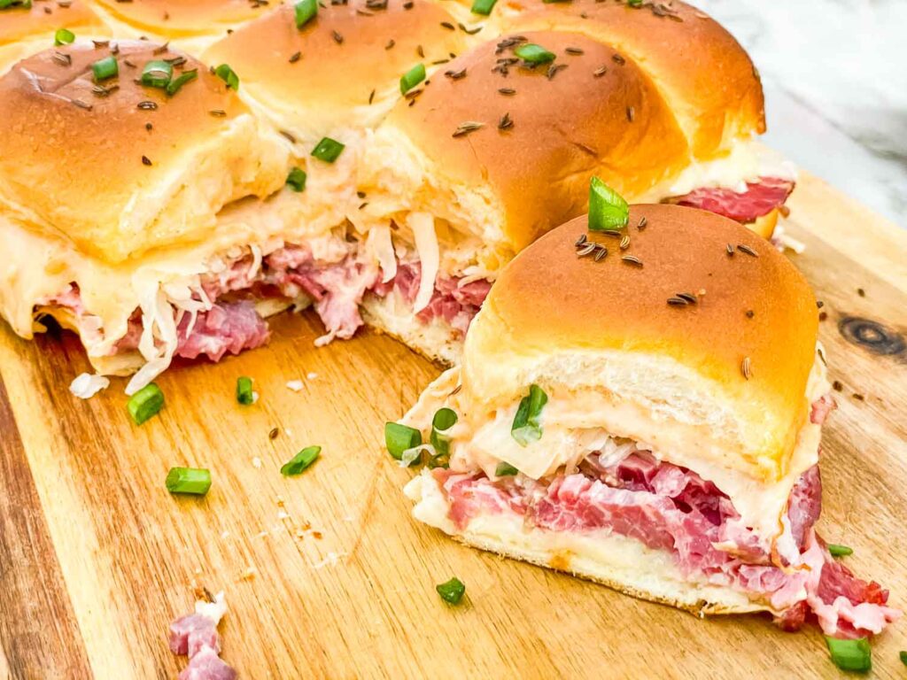 A single Corned Beef Reuben Slider in front of the rest on a cutting board.