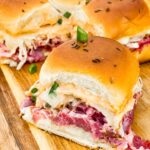 A single slider in front of other Corned Beef Reuben Sliders on a cutting board.