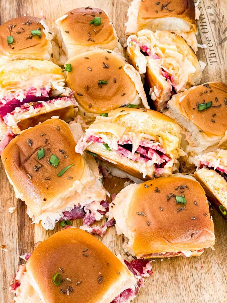 A pile of Corned Beef Reuben Sliders on a wood board.