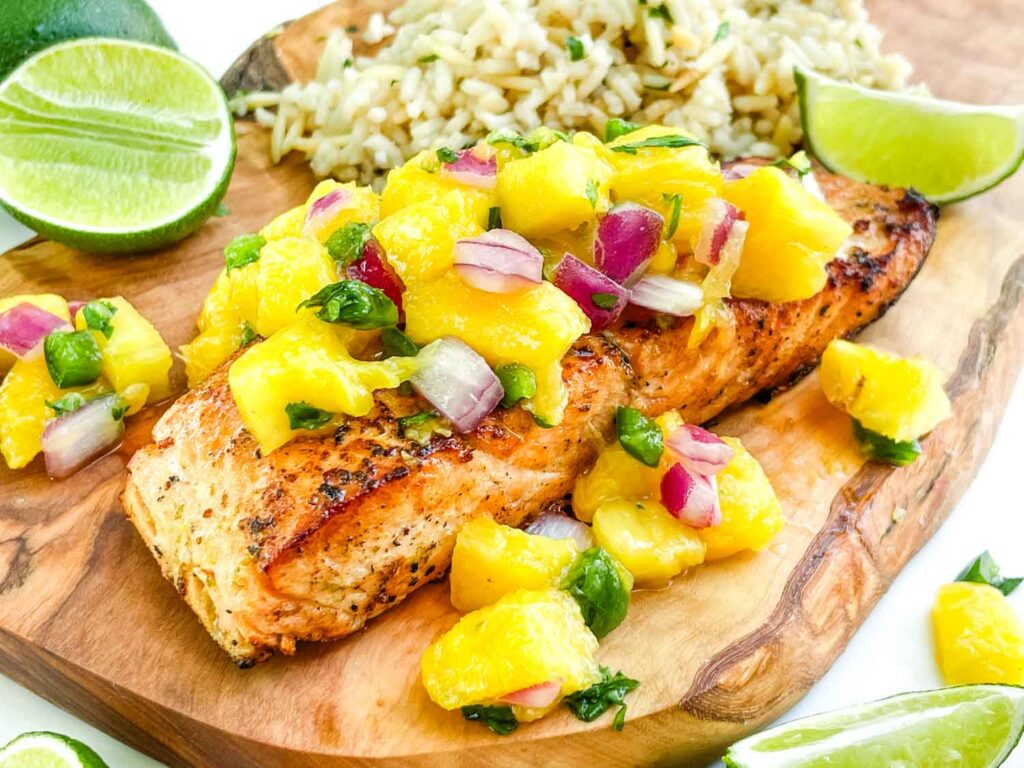 A piece of Salmon with Mango Salsa sitting on a wood board.