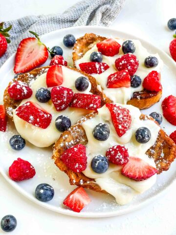 Looking down on a white plate with three Mixed Berry French Toast pieces and fresh berries.
