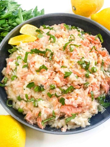 Looking down on a bowl of Salmon Risotto with fresh lemons around it.