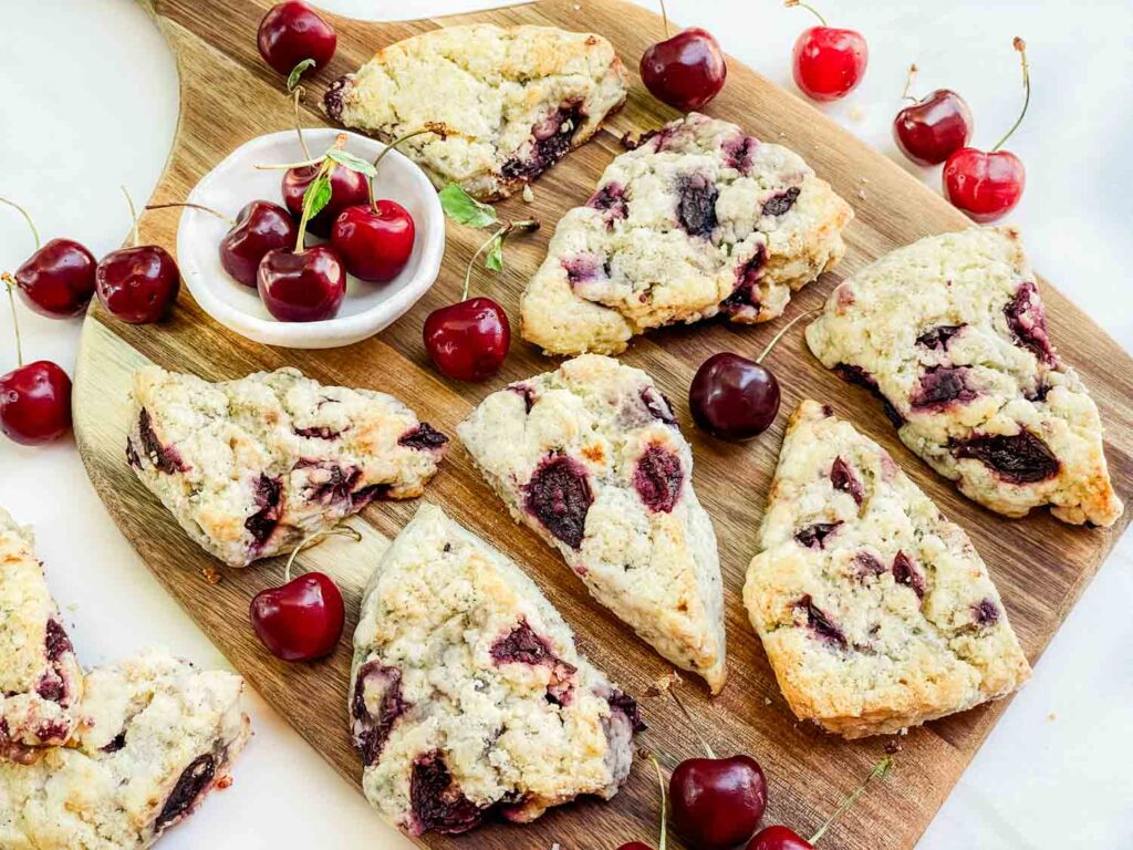 Looking down on Simple Cherry Scones on a wood board surrounded by fresh cherries.