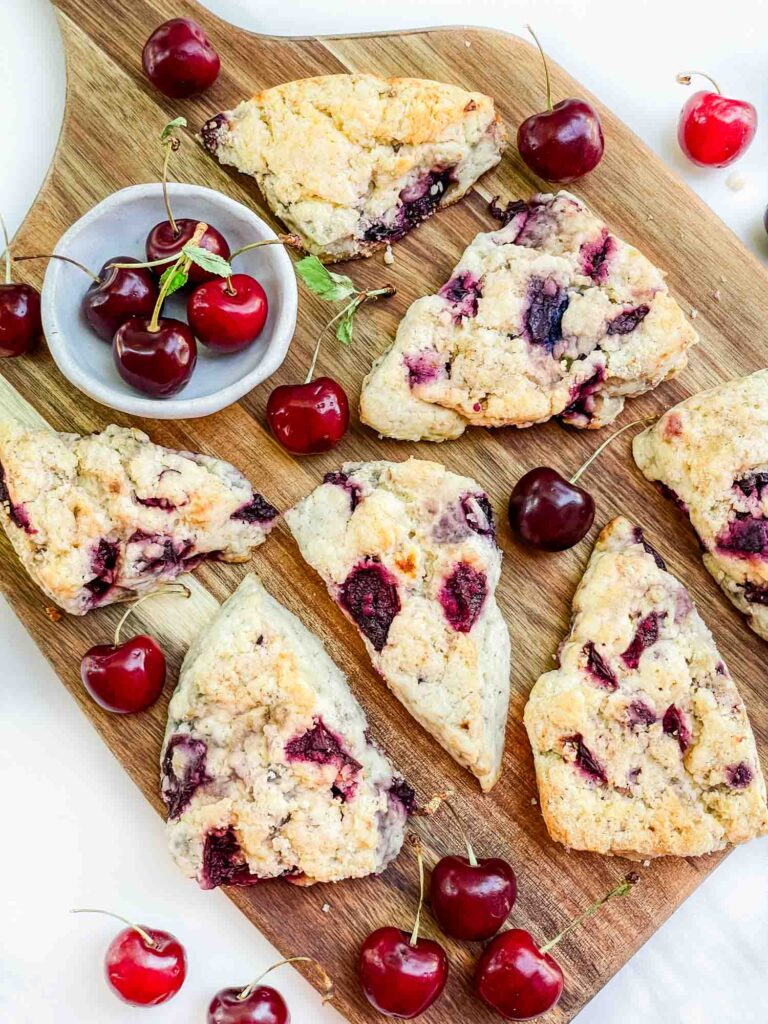 Looking down on a wood board full of Simple Cherry Scones with fresh cherries around them.