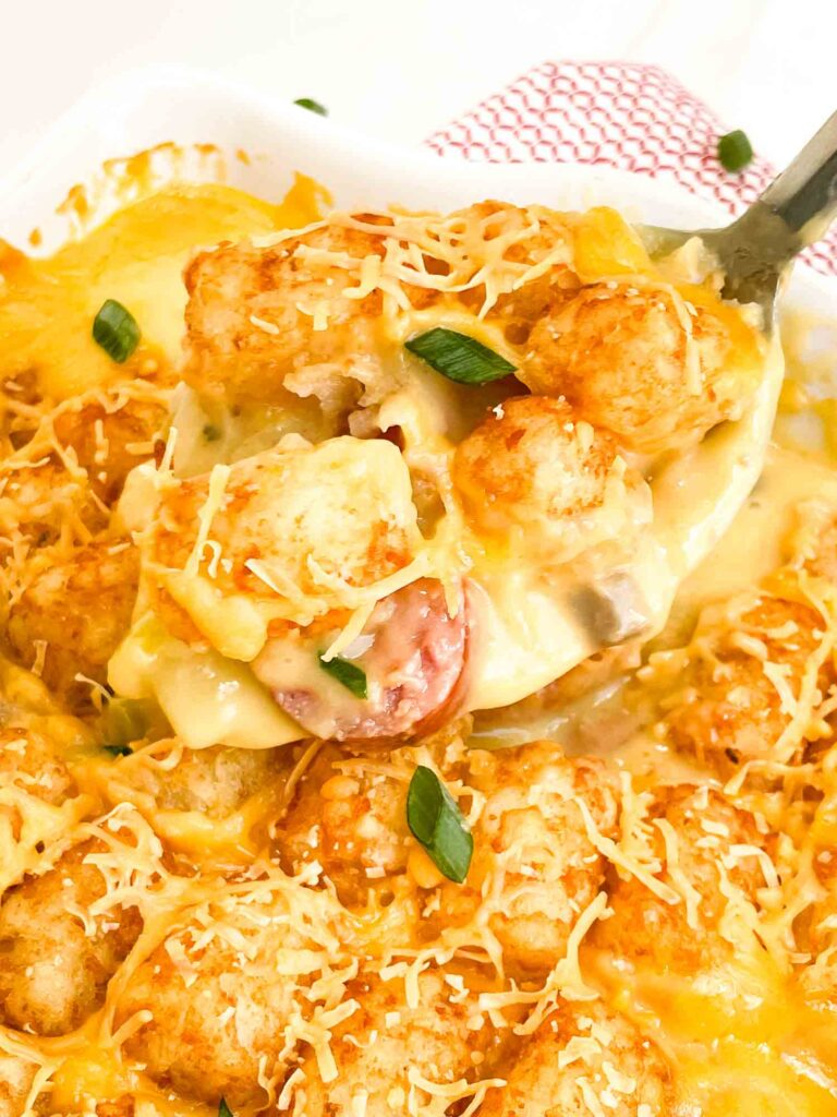 A serving spoon scooping Tim Walz's New Ulm Hotdish with Brats out of the baking dish.