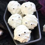 Mummy Cake Pops piled in a ceramic coffin dish.