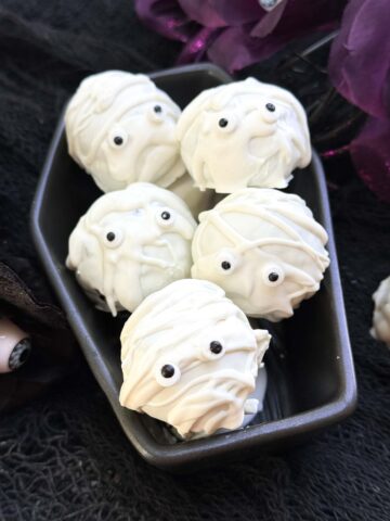 Mummy Cake Pops piled in a ceramic coffin dish.