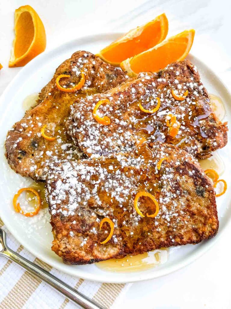 Looking down on three pieces of Panettone French Toast Recipe on a plate with orange zest and pieces.