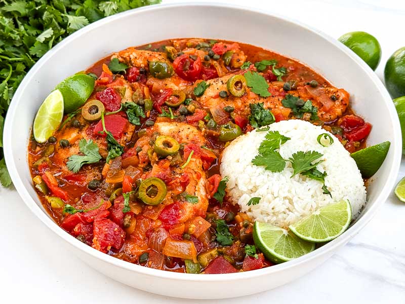 A shallow bowl full of Chicken Veracruz (Pollo a la Veracruzana) with some white rice, sitting on a counter.