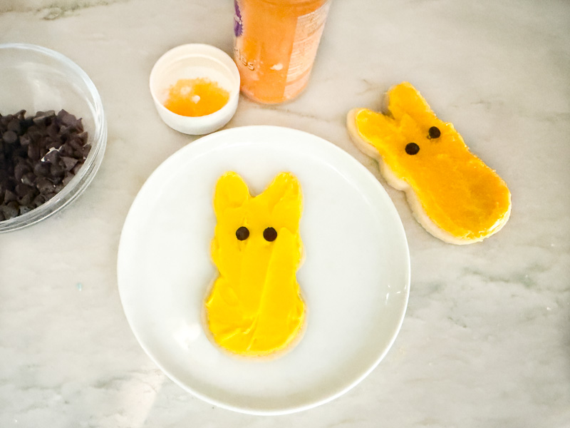 A cookie being frosted with yellow icing on a small plate on the counter.