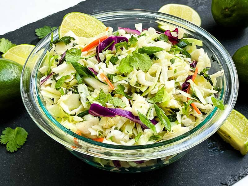 A glass bowl full of Cilantro Lime Coleslaw on a black stone.
